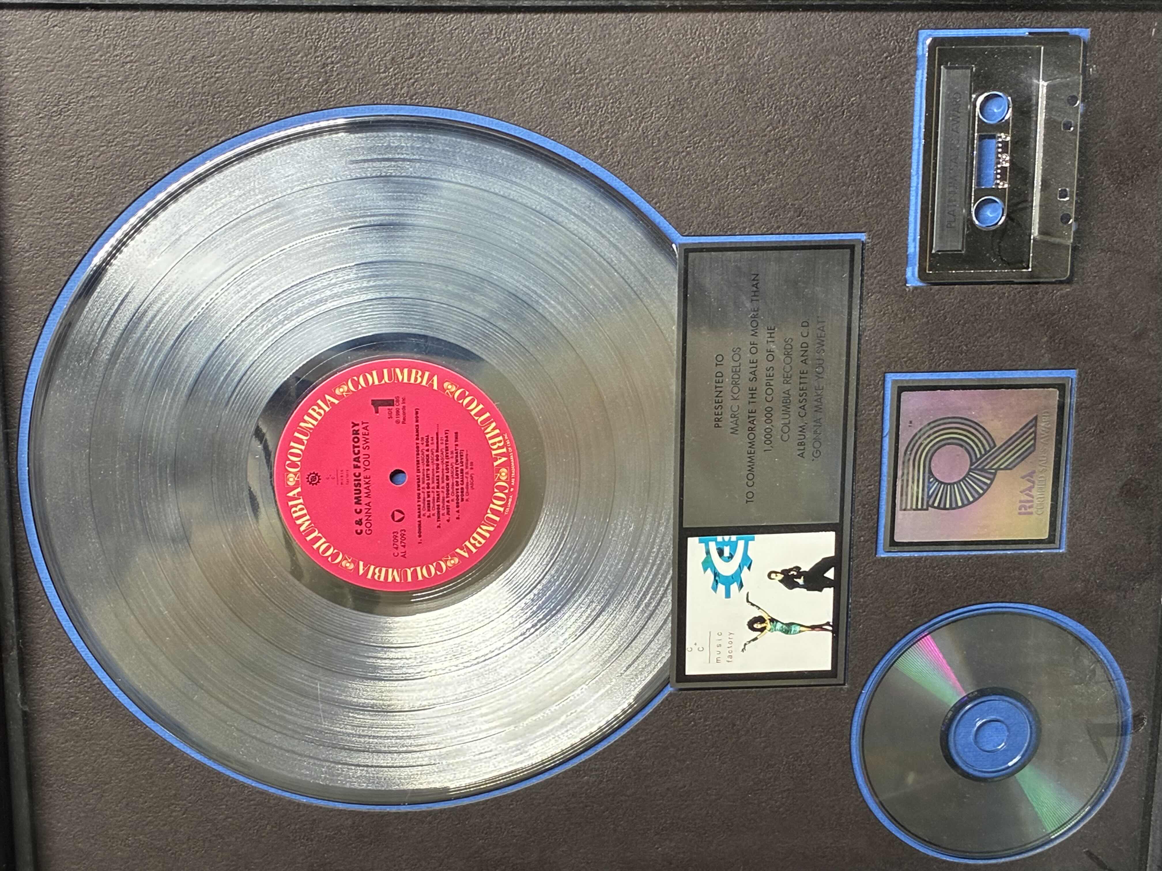 Photo 1 of PLATINUM RECORD PRESENTED TO MARC KORDELOS TO COMMEMORATE THE SALE OF MORE THAN $1M COPIES OF THE COLUMBIA RECORDS ALBUM, CASSETTE & CD
"GONNA MAKE YOU SWEAT" FRAMED PLAQUE 17“ X 21“
