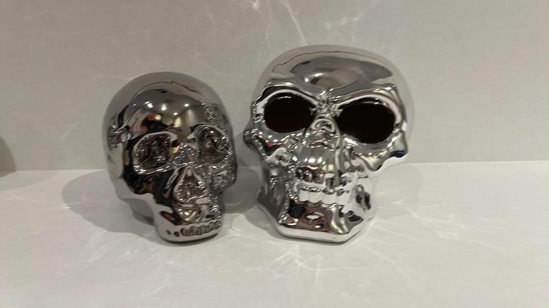 Photo 1 of 2-SILVER CERAMIC SKULLS. SMALLER ONE IS A PIGGY BANK, H5” LARGER SKULL LIGHTS UP, H6”