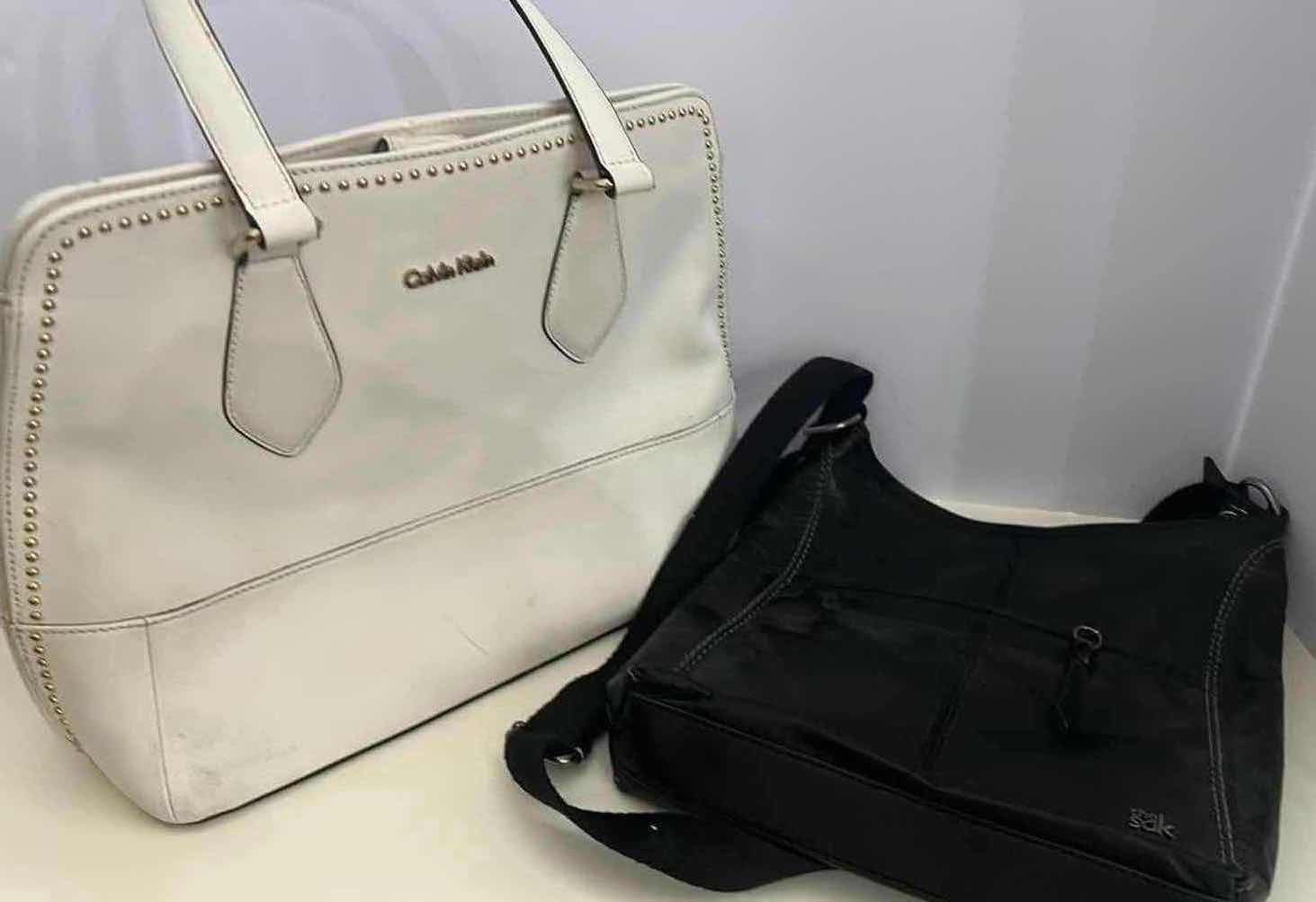Photo 1 of 2- DESIGNER PURSES. WHITE "CALVIN KLEIN" AND  BLACK "THE SAK" BAGS.