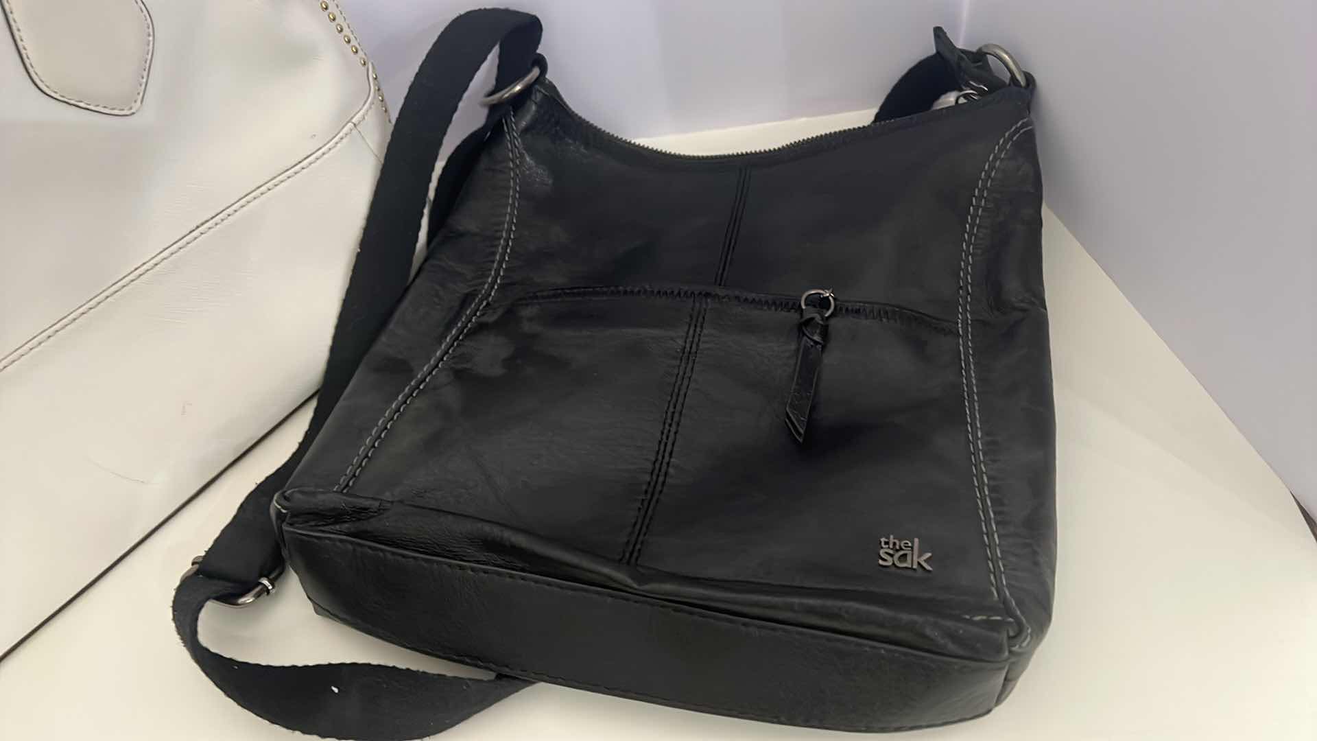 Photo 1 of 2- DESIGNER PURSES. WHITE "CALVIN KLEIN" AND  BLACK "THE SAK" BAGS.