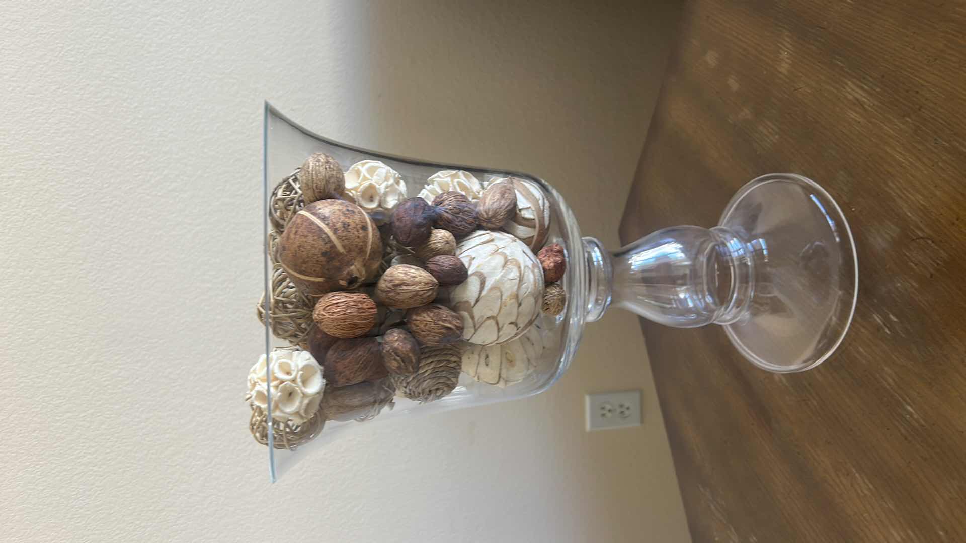 Photo 1 of CLEAR GLASS PEDESTAL VASE FILLED WITH DECORATIVE NATURAL BOTANICAL PODS AND ORBS. 
H15”