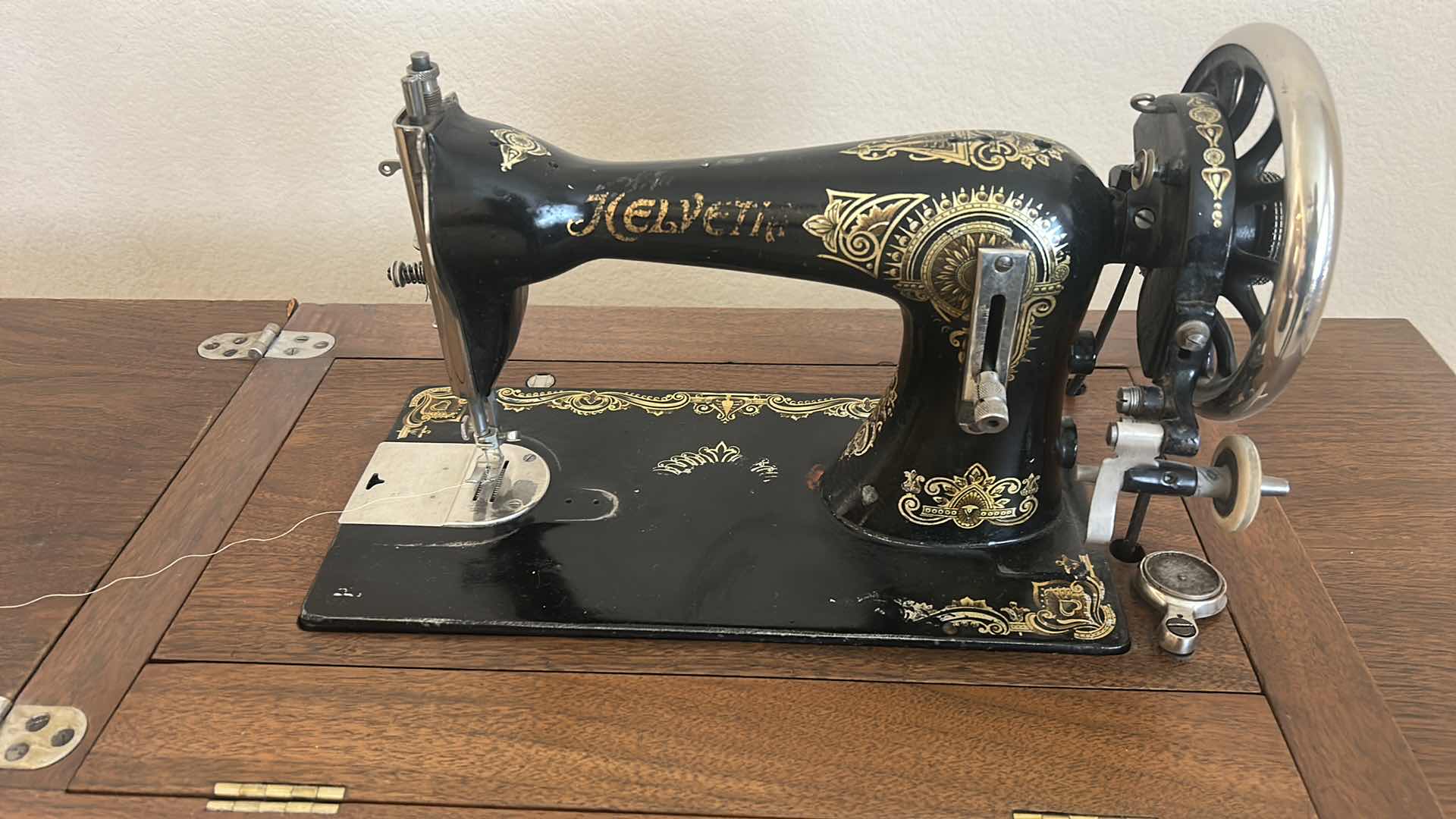 Photo 1 of ANTIQUE HELVETIA TREADLE SEWING MACHINE AND CABINET, ORNATE CAST IRON AND GOLD DETAILING PLUS PARTS. INCLUDES CAST IRON TREADLE BASE, SEWING MACHINE HEAD, WOOD TABLE TOP, DRAWERS, AND LOOSE WOOD COMPONENTS. 
36 1/2“ x 18 1/2“ x H32“