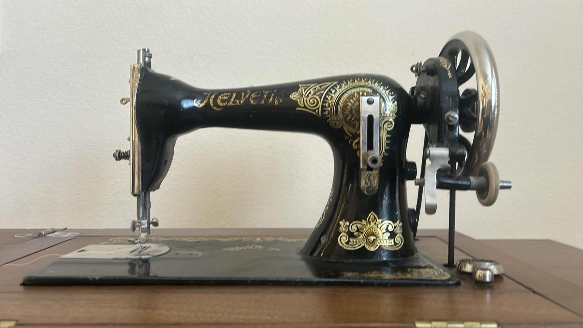 Photo 1 of ANTIQUE HELVETIA TREADLE SEWING MACHINE AND CABINET, ORNATE CAST IRON AND GOLD DETAILING PLUS PARTS. INCLUDES CAST IRON TREADLE BASE, SEWING MACHINE HEAD, WOOD TABLE TOP, DRAWERS, AND LOOSE WOOD COMPONENTS. 
36 1/2“ x 18 1/2“ x H32“