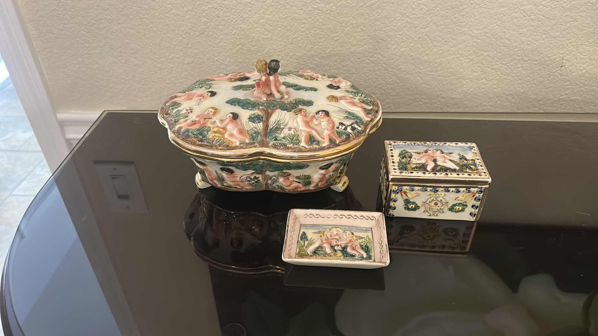 Photo 1 of ANTIQUE CAPODIMONTE ITALIAN PORCELAIN DRESSER SET FEATURING RAISED RELIEF DESIGNS OF CHERUBS .
•THE SET INCLUDES A LARGE LIDDED BOX, A SMALLER LIDDED JEWELRY BOX, AND A SMALL OPEN TRAY.   LARGEST 9 1/4” x 7 1/4” x H5 1/2”
