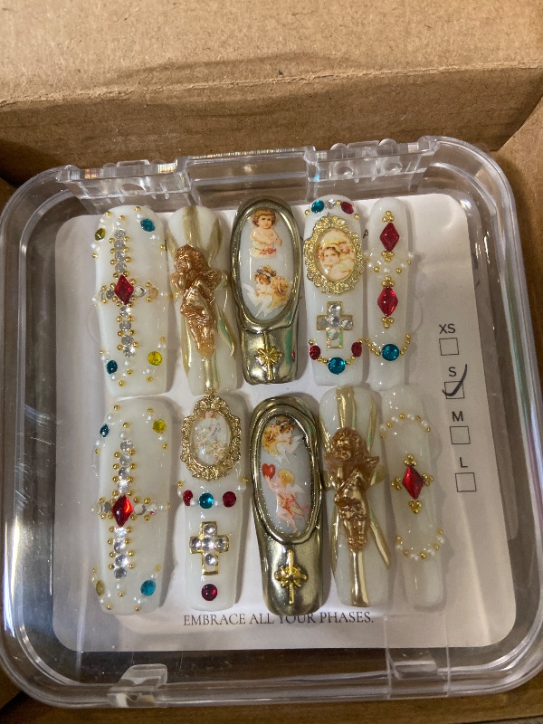 Photo 1 of Baroque-inspired press-on nails featuring a white base with gold alloy angel charms, gemstone crosses, and cherub portraits