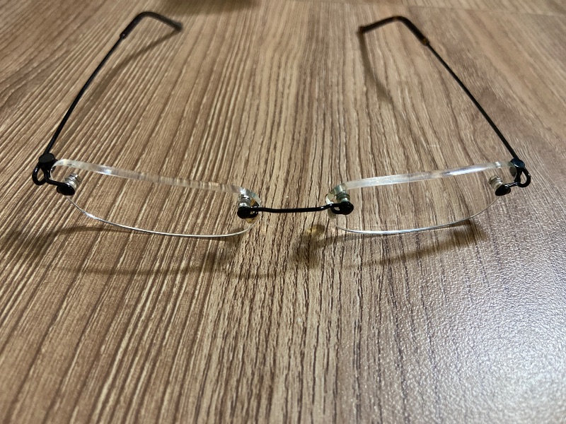 View 1 of +1.25 rimless reading glasses feature a minimalist, frameless rectangular design with sleek black metal temple arms and screw-mount connections.