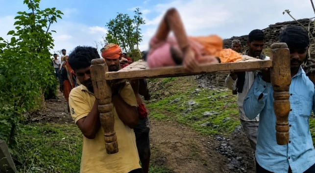 Villagers carrying a pregnant woman on a cot across a rural path