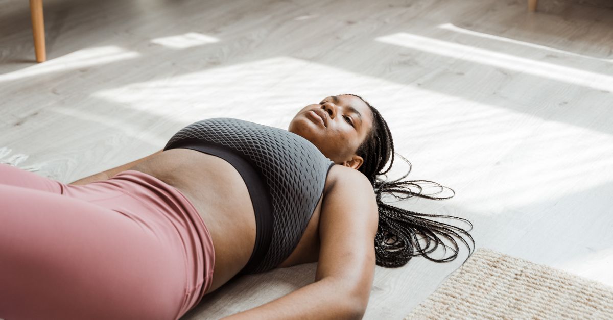Woman in activewear relaxing on a gym mat indoors, highlighting self-care and fitness.