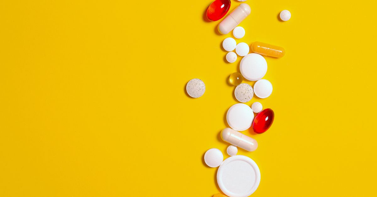Assorted pills and capsules scattered on a bright yellow background, representing healthcare and medication.