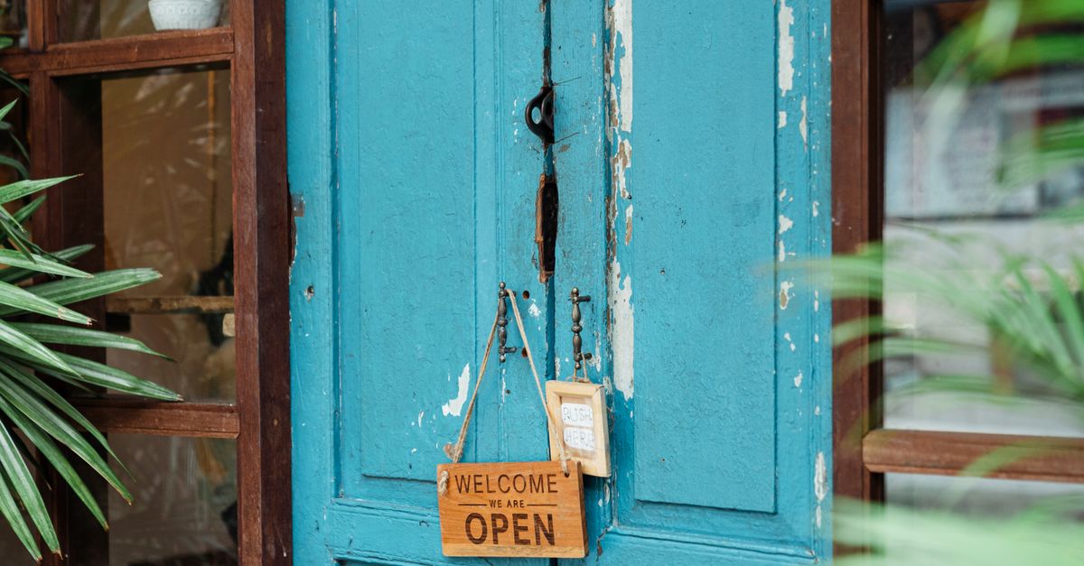 A rustic blue door with a wooden welcome sign showcasing an open establishment.