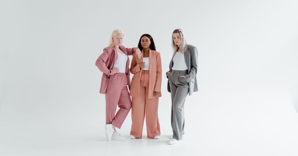Three diverse women pose confidently in pastel business suits against a white background.