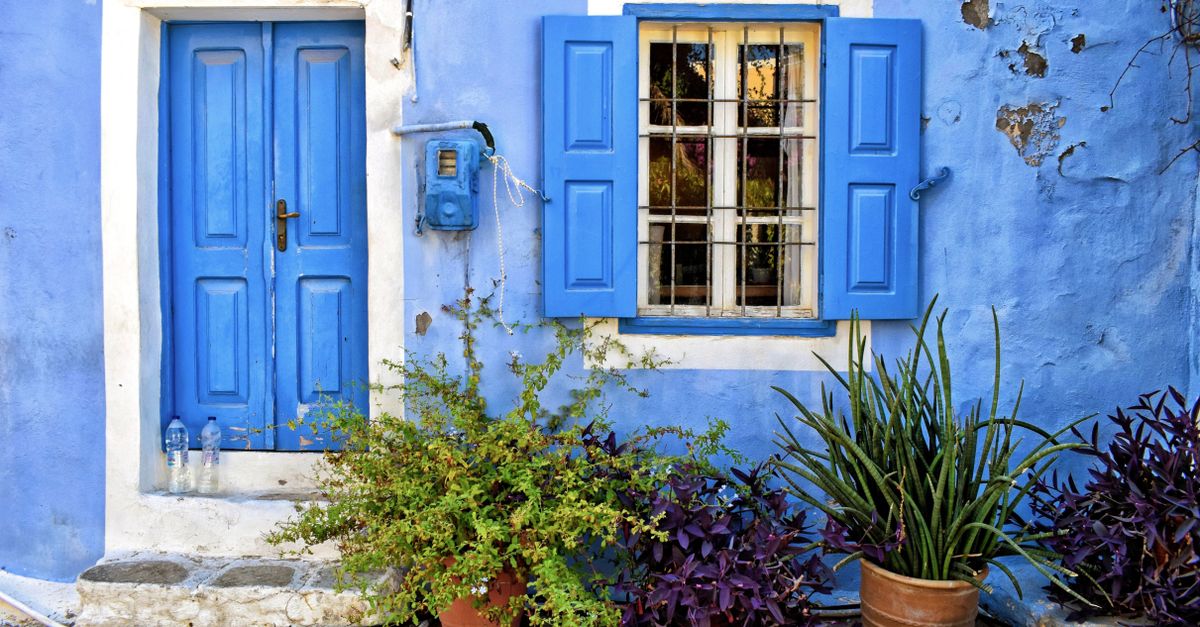 Explore the captivating blue facade decorated with potted plants in Ano Symi, Greece.