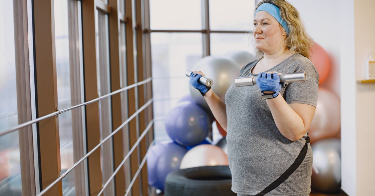 Woman in gym with dumbbells by a window, highlighting fitness and lifestyle.