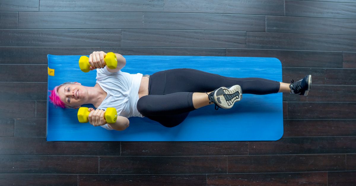 A woman working out with dumbbells on a yoga mat in a gym setting indoors.