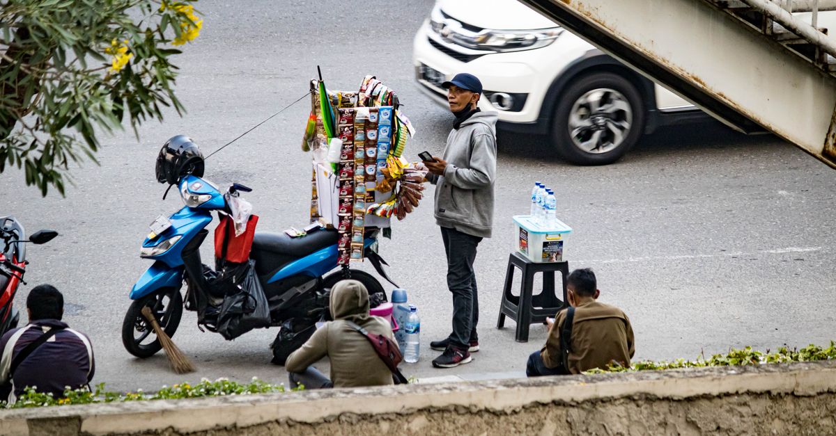 Street vendor beside a motorcycle selling snacks and drinks on a busy city street.