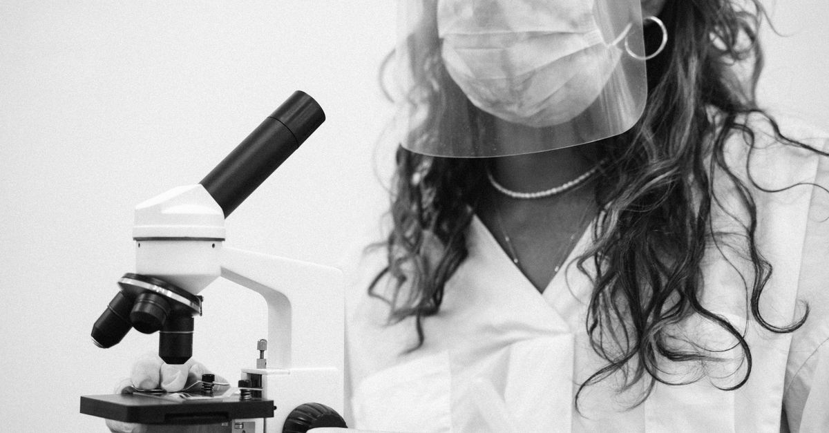 A scientist wearing protective equipment examines a sample using a microscope.