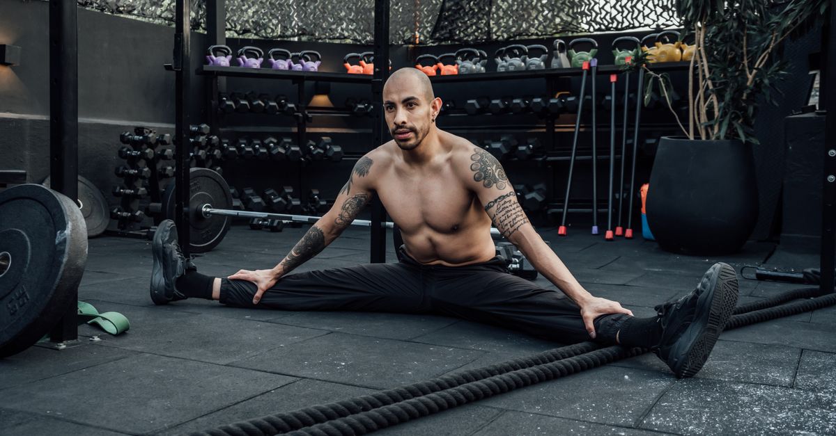 Tattooed man performing a split stretch in a gym, showcasing flexibility and fitness lifestyle in Mexico City.