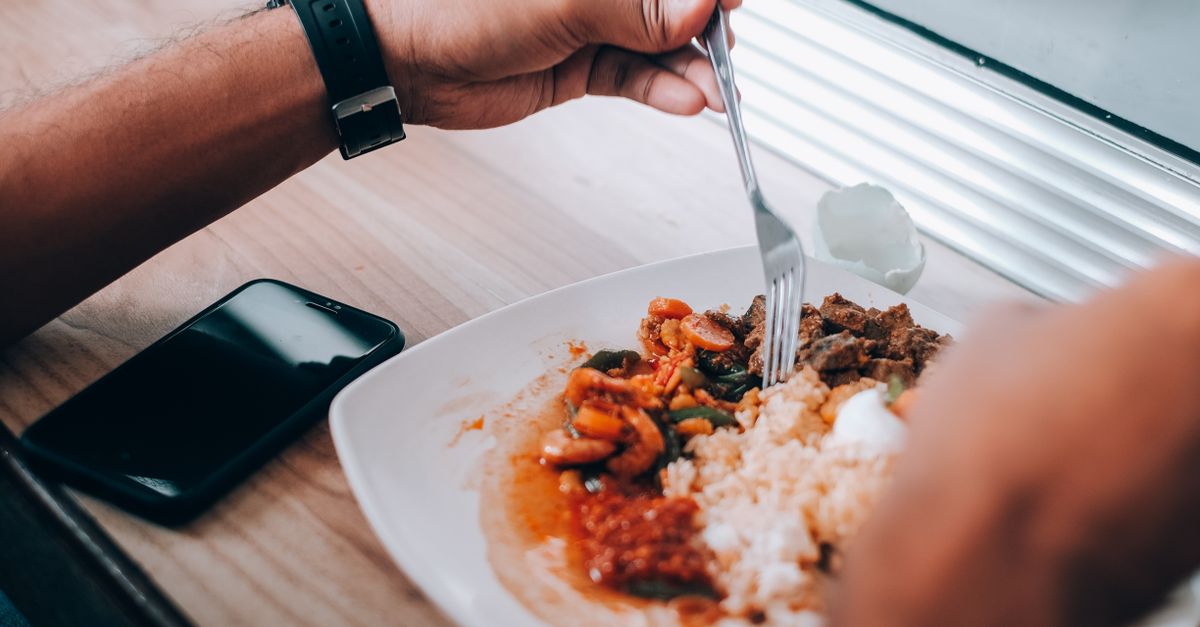 A person enjoys a meal of rice with mixed vegetables by a window.