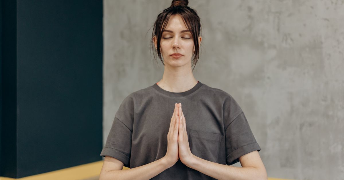 A woman meditating indoors with eyes closed, focusing on mindfulness and relaxation.