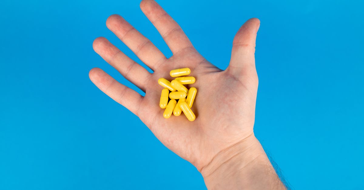 A close-up of a hand holding yellow capsules against a vibrant blue background.