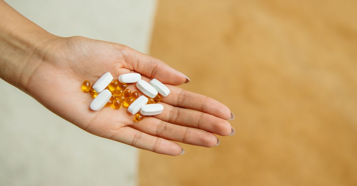 Close-up of a hand holding white pills and yellow capsules, symbolizing health and wellness.