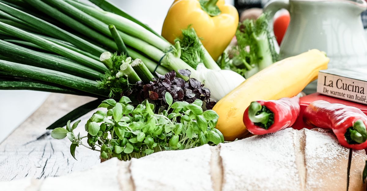 A vibrant assortment of fresh vegetables, herbs, and bread on a rustic surface, ideal for culinary scenes.