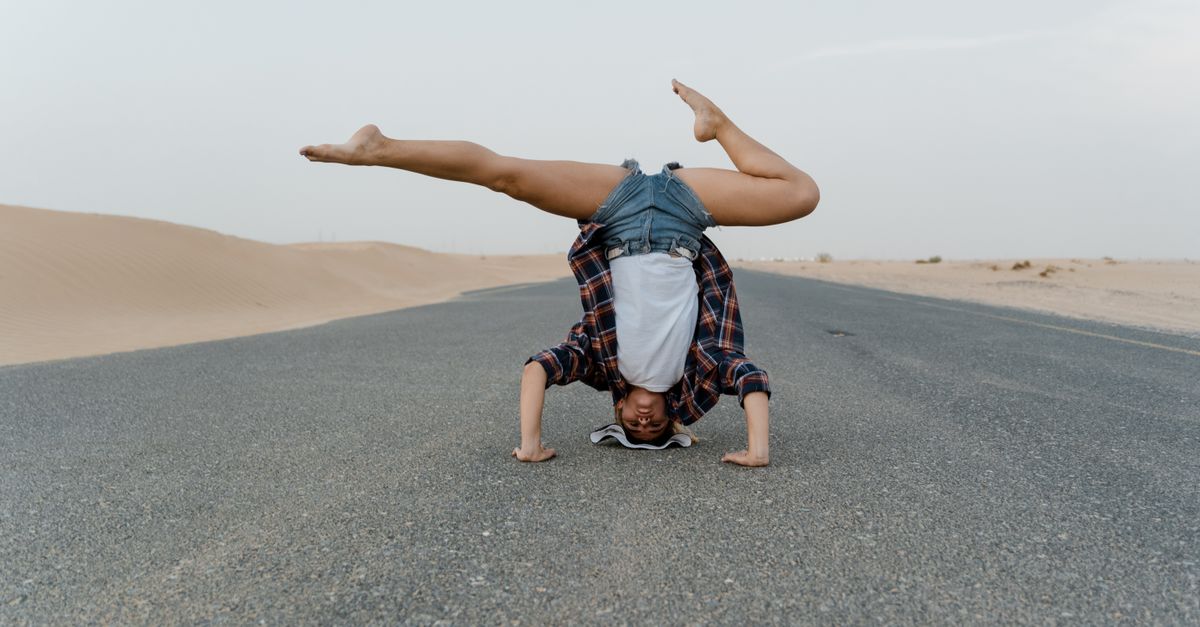 Woman performing a headstand on an asphalt road amid sand dunes. Outdoor setting.