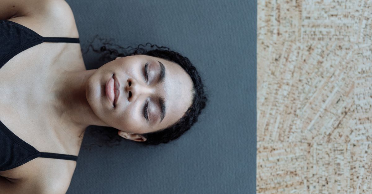 A serene portrait of a woman with curly hair lying on a yoga mat indoors, exuding calmness.
