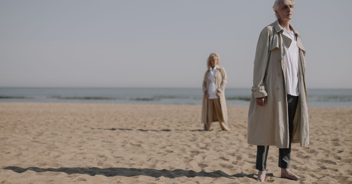 Elderly couple enjoying a summer day at the beach in stylish trench coats, capturing a serene and romantic moment.