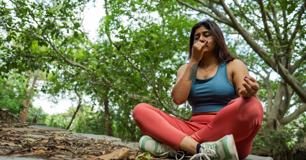 Young woman meditating in a forest, practicing yoga breathing exercises on a stone platform.