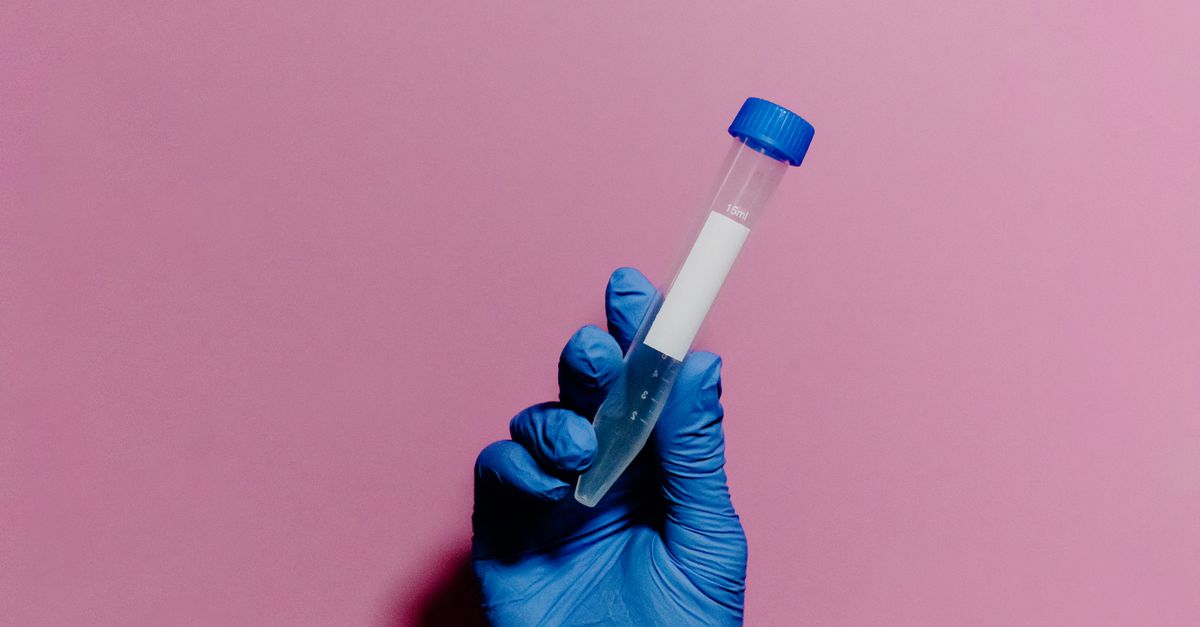 Blue gloved hand holds a test tube against a pastel pink background, emphasizing medical themes.