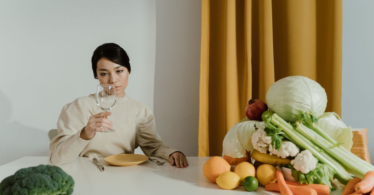 A woman sitting at a table with fresh vegetables, contemplating a wine glass.
