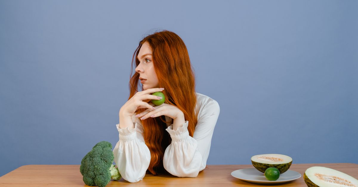 Thoughtful woman with broccoli, melon, and lime on a table.