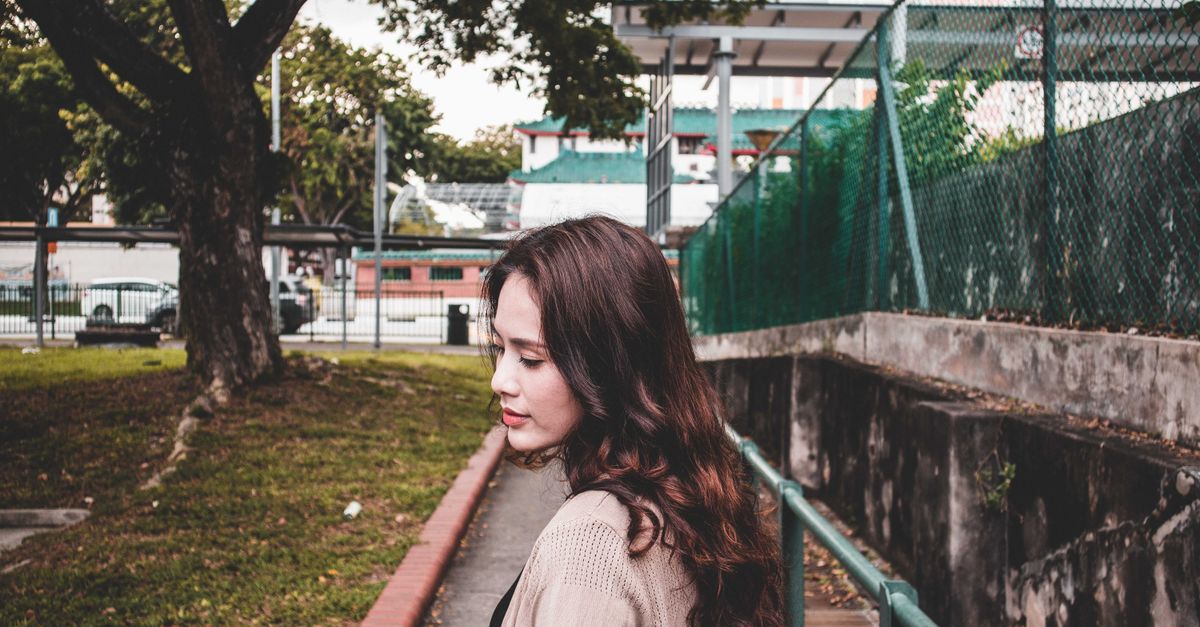 A young woman with curly hair walks along a pathway in a park, showcasing a thoughtful expression.