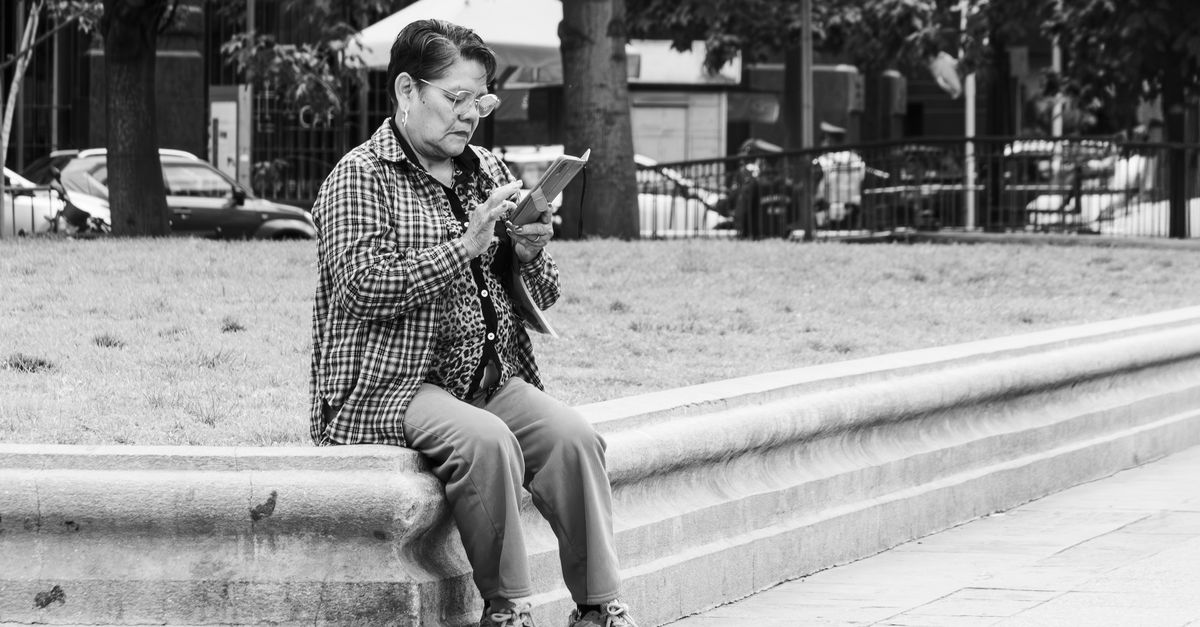 Black and white photo of a senior woman using a tablet on a park bench in Santiago, Chile.