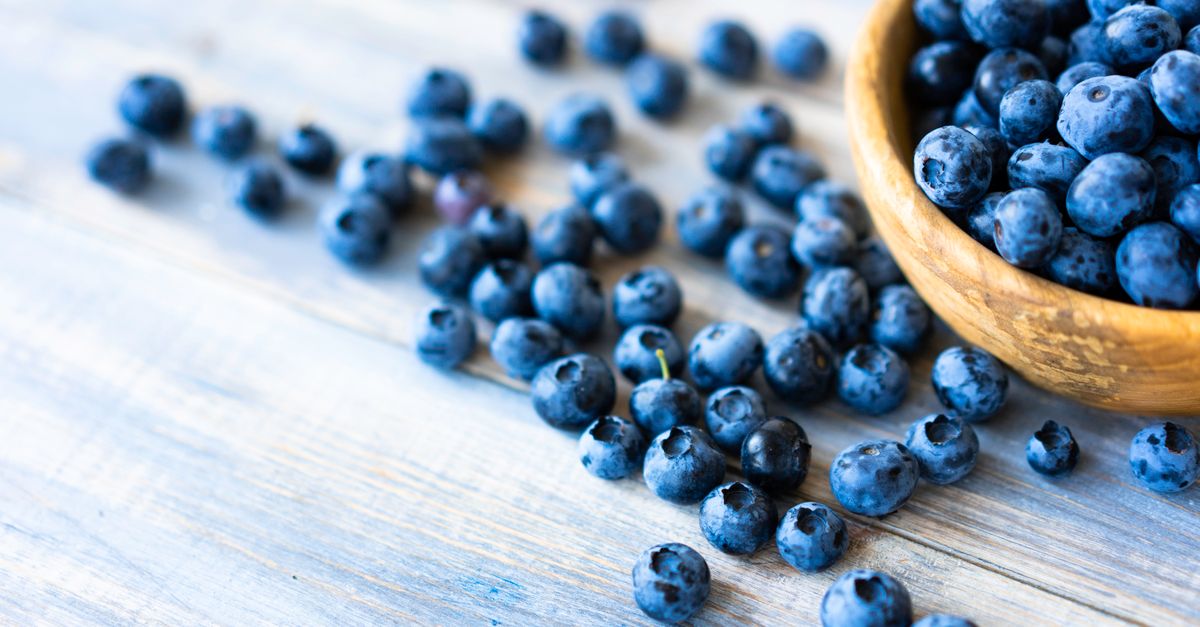 A close-up of fresh blueberries spilling from a wooden bowl on a rustic wooden table.