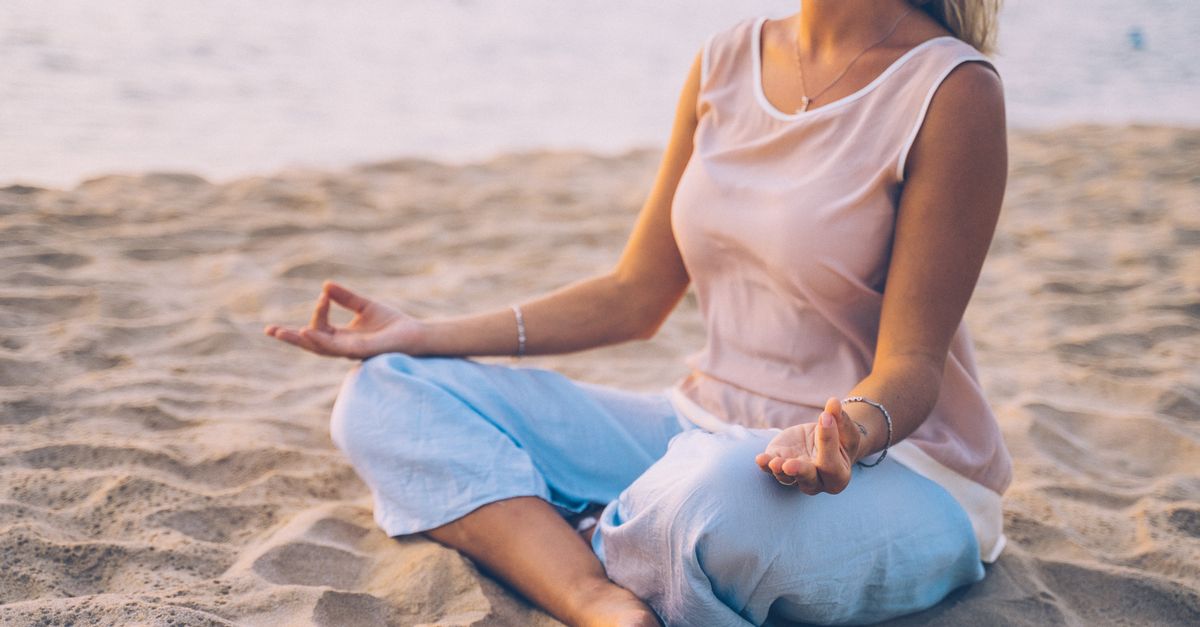 Woman practicing yoga in lotus pose on a sandy beach at sunset.