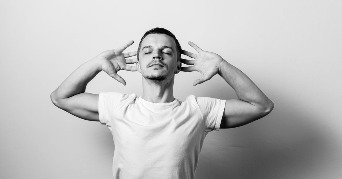 Black and white portrait of a serene man with hands on head, eyes closed.