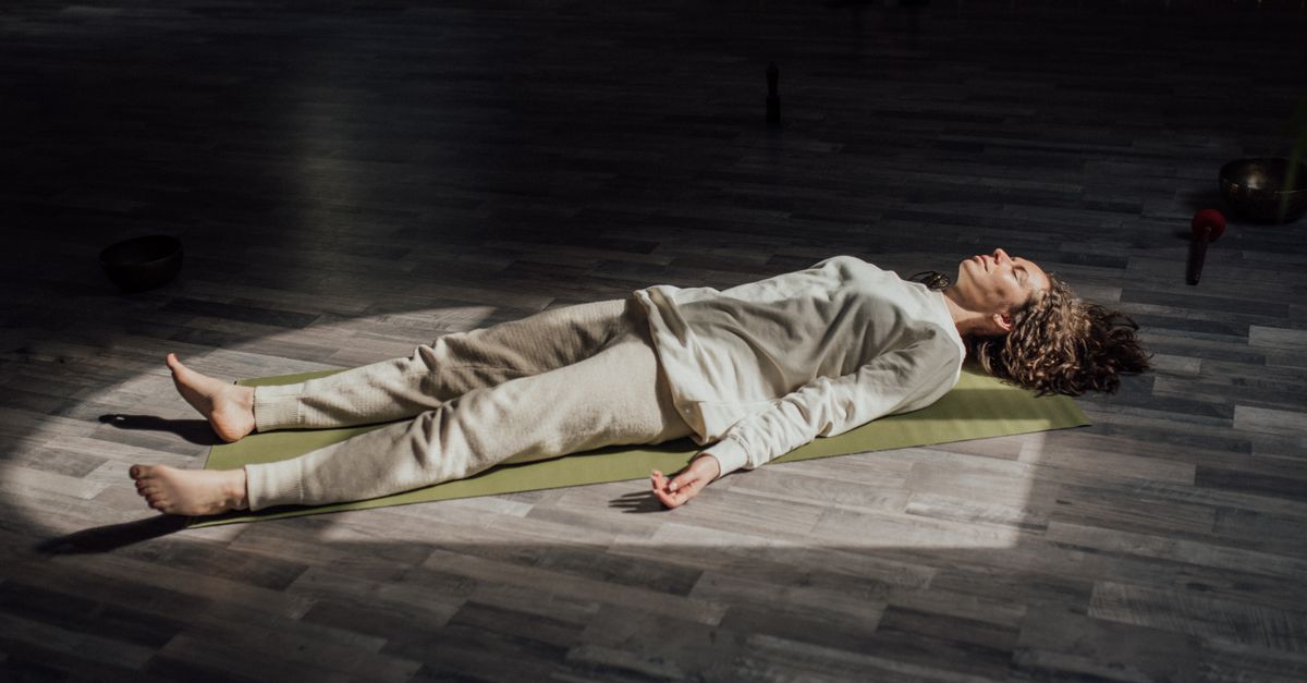 Woman lying on a yoga mat indoors, meditating and relaxing in a calm setting.
