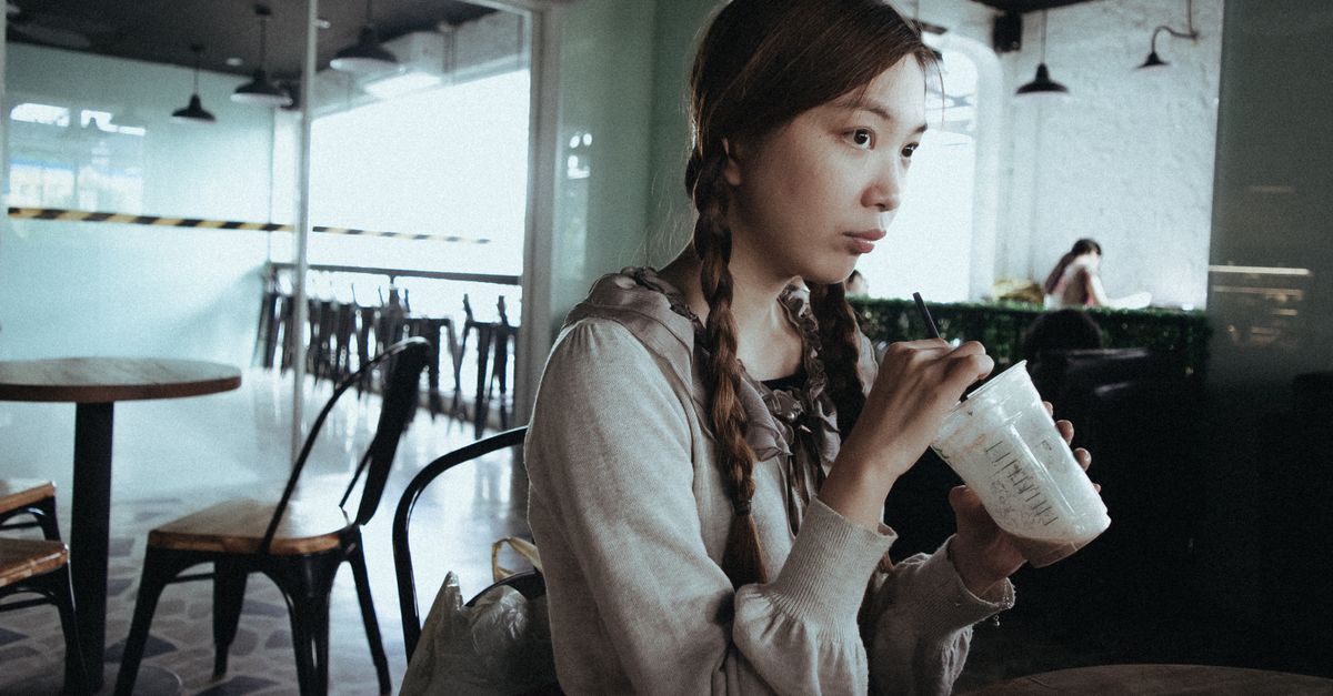 A woman with braids sipping a drink in a cozy café setting, captured from the front.