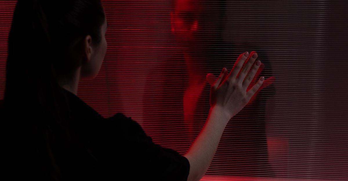 A woman reaches towards her own reflection, illuminated by a dramatic red light.