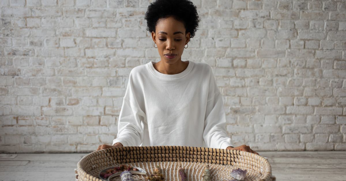 A woman in a white sweater meditates with a basket of crystals, symbolizing spirituality and relaxation.