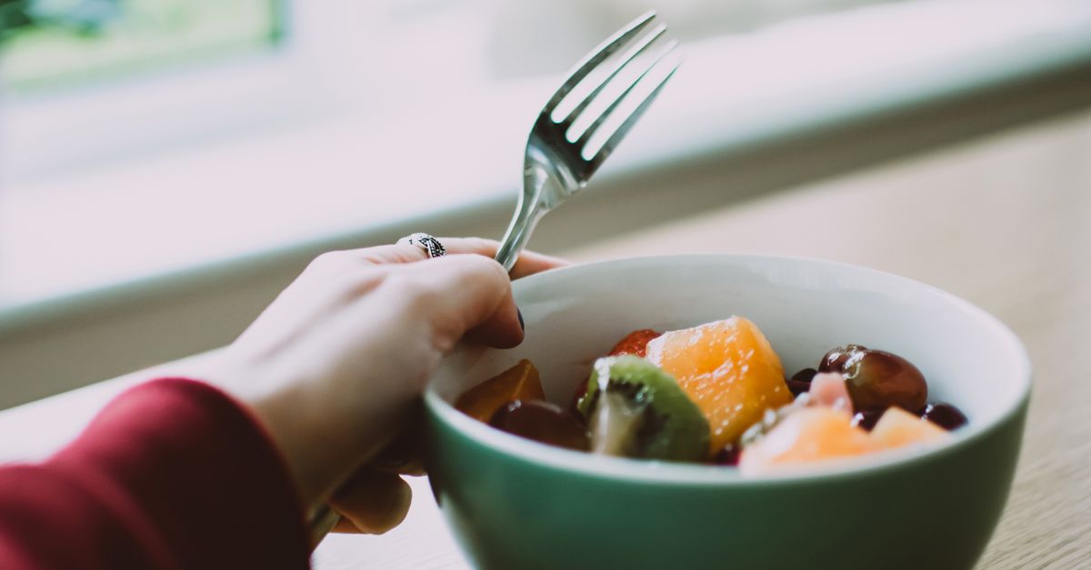 Close-up of a fruit salad bowl with a hand holding a fork in a well-lit indoor setting.