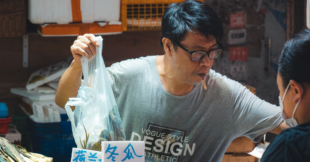 A vendor in a Hong Kong street market selling fresh vegetables to customers.