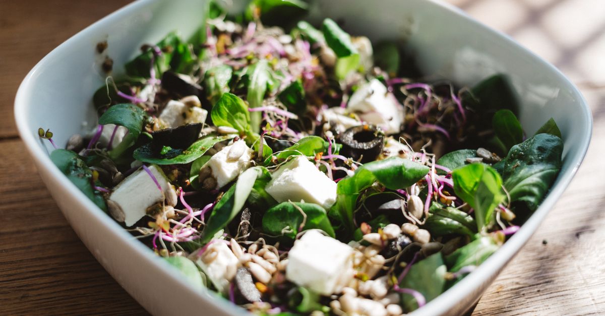 Fresh spinach salad with feta, olives, and sprouts, served in a sunlit bowl.
