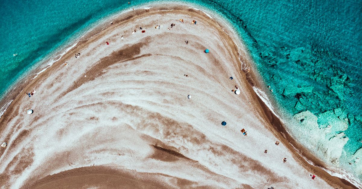 A breathtaking aerial shot of a sandy beach with turquoise waters, showcasing beachgoers and umbrellas.