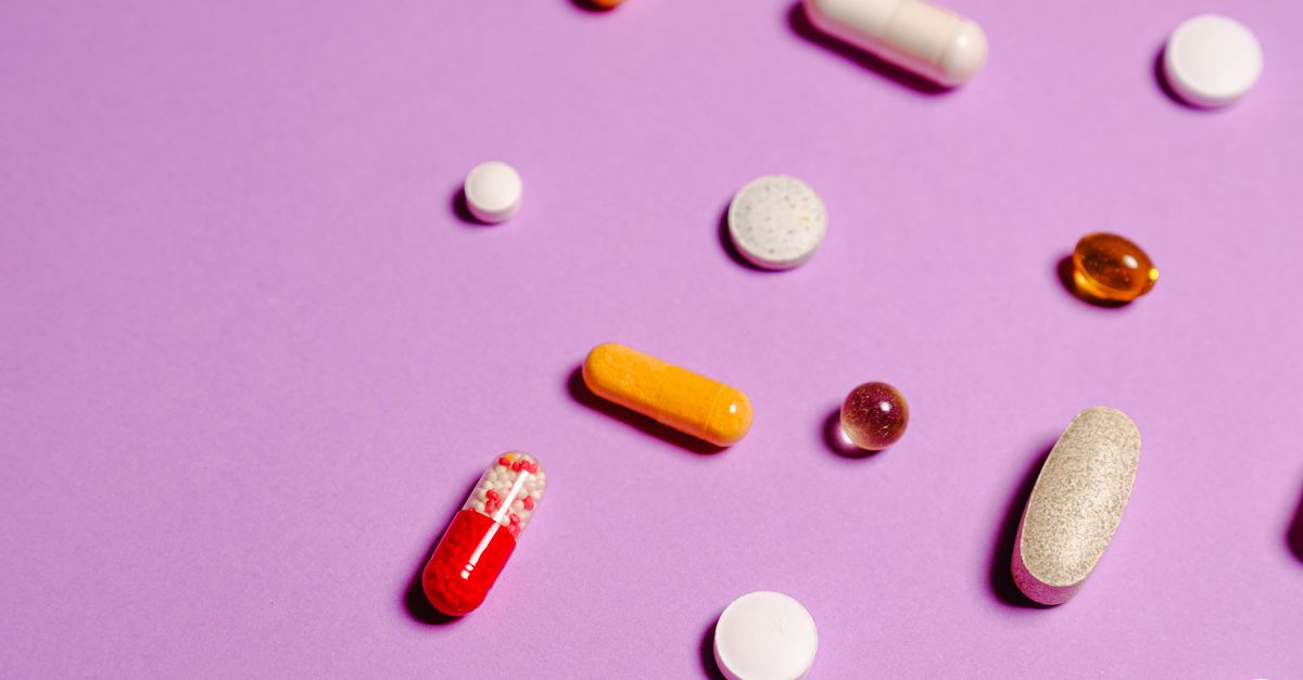 A vibrant flat lay of various pills and capsules on a purple surface.