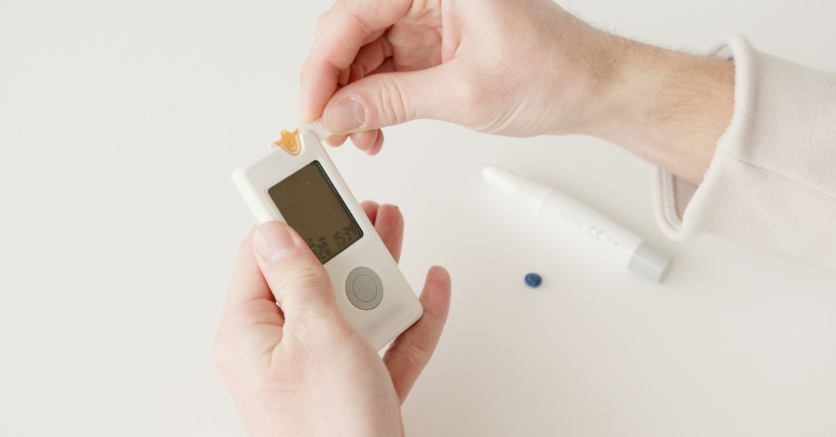 Close-up image of hands checking blood glucose level using a glucometer, featuring testing supplies on a white background.