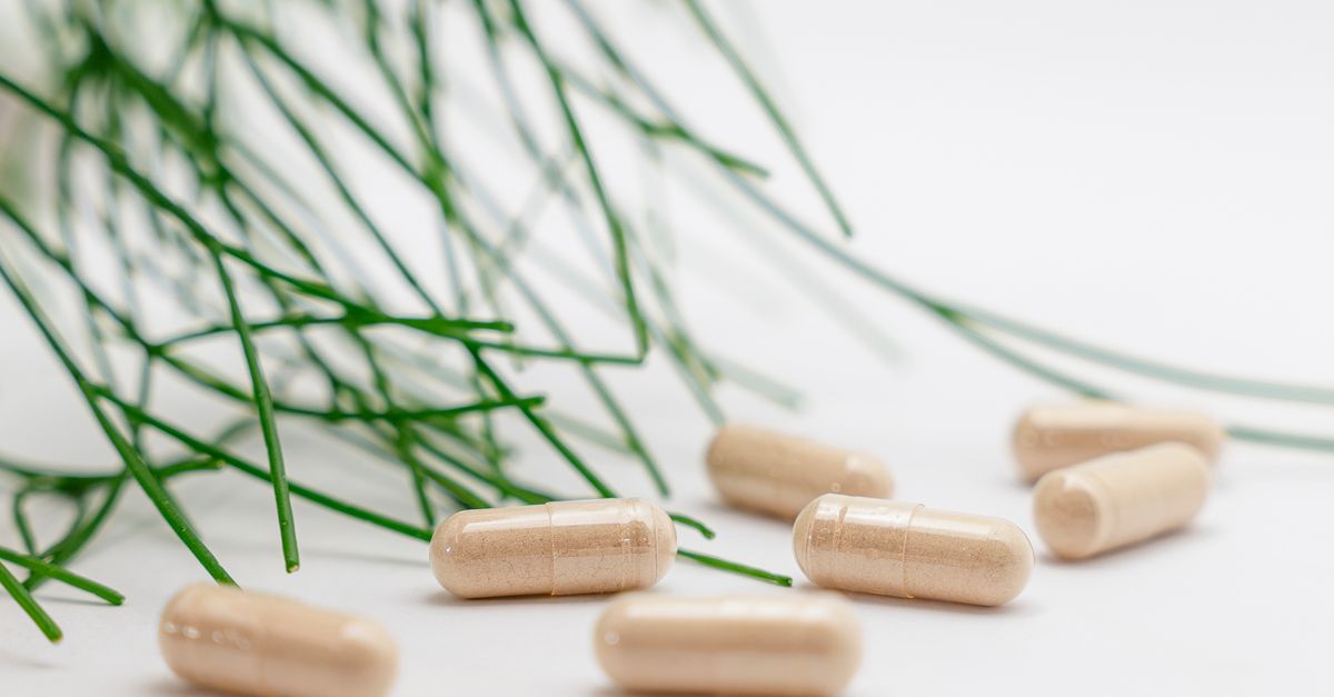 Natural herbal supplement capsules with green leaves on a white background.