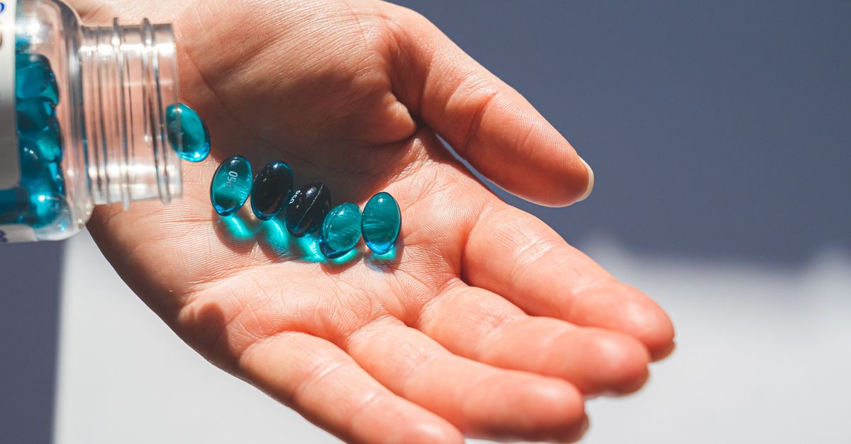 Blue gel capsules pouring from a bottle into an open hand, showcasing medication concept.